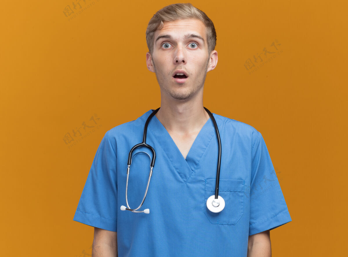 制服惊讶的年轻男医生穿着医生制服听诊器隔离在橙色墙上医生惊喜穿