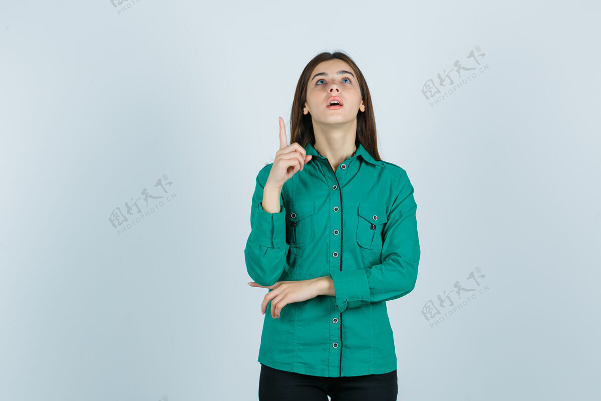 衬衫年轻的女性指着绿色的衬衫 看着好奇 前视图人女士华丽