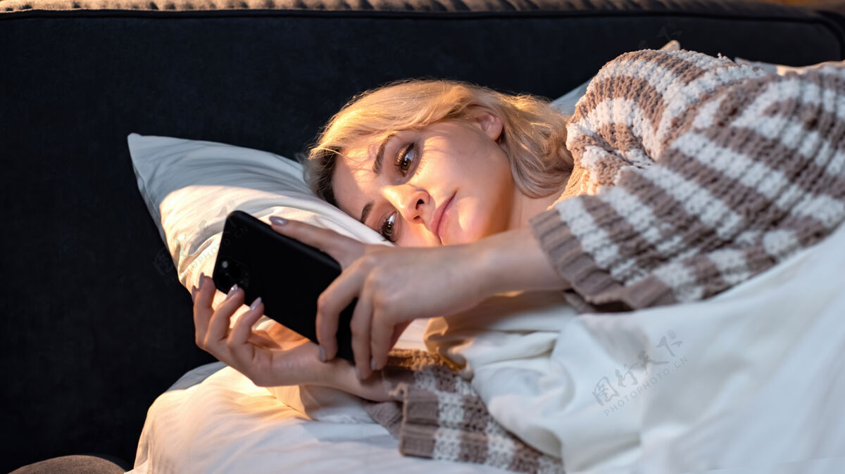 电话年轻的金发女孩在床上用她的智能手机试图入睡社交媒体成瘾卧室女人抱着