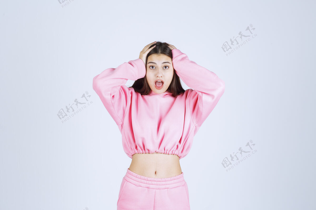 成人一个穿着粉色睡衣的女孩抱着她的头 因为她精疲力尽或头痛年轻模特生病