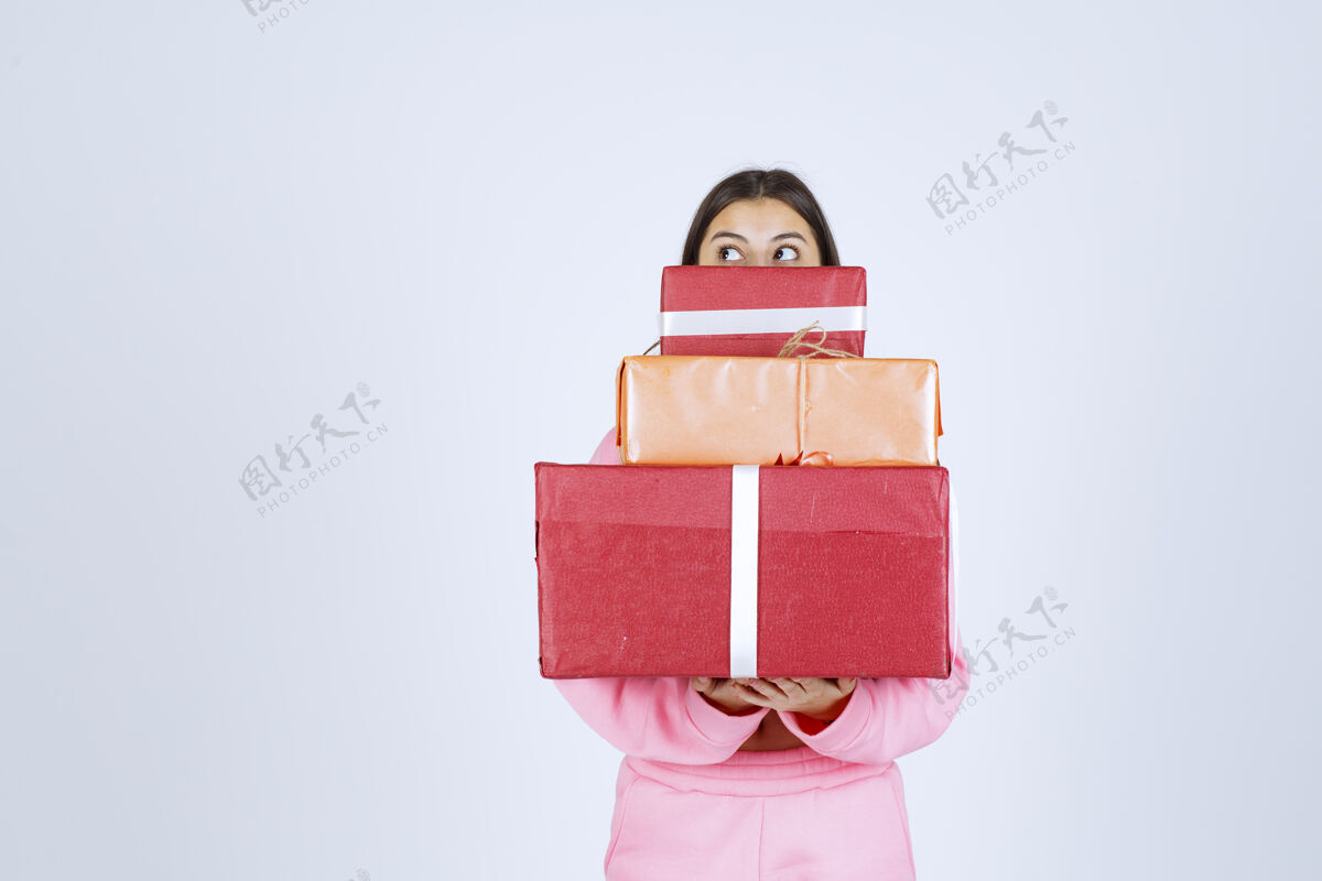 人类穿着粉色睡衣的女孩手里拿着多个红色礼盒 把脸藏在礼盒后面雇员堆模特