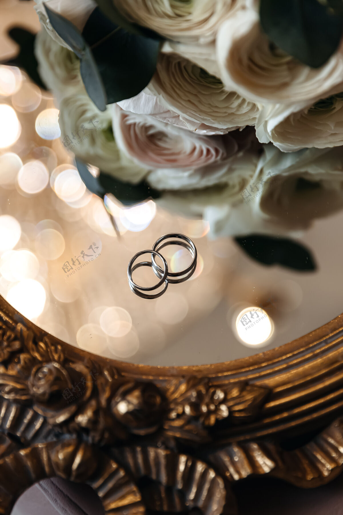情侣新娘和新郎的结婚戒指放在镜子表面 旁边有鲜花银戒指节日