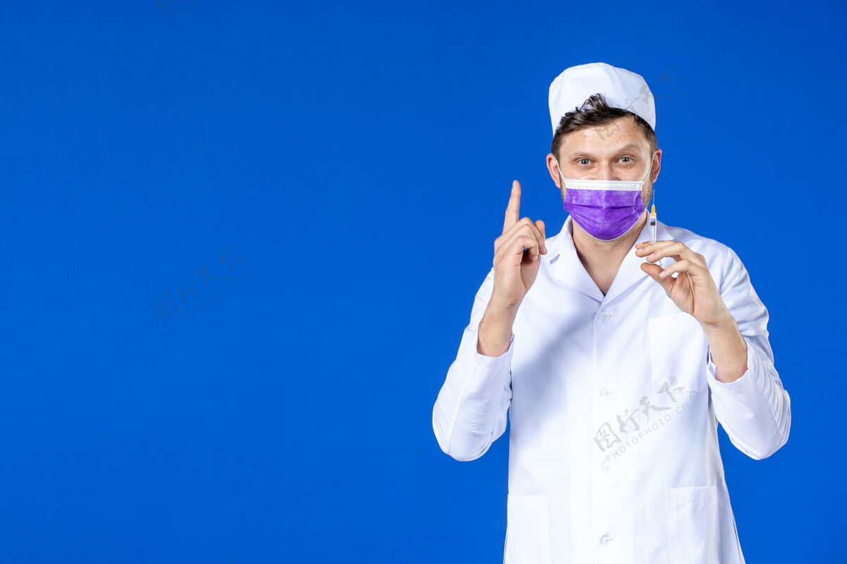 大流行身穿医疗服 戴着紫色口罩的男医生正对着蓝色的脸拿着针剂治疗病毒药品