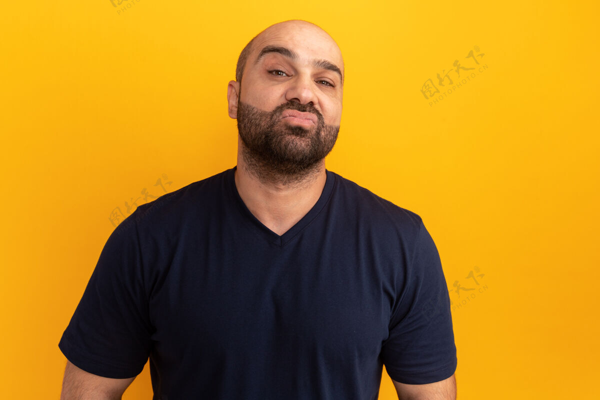 男人身着海军t恤的留胡子男人站在橙色的墙上 表情严肃自信严肃站立表情