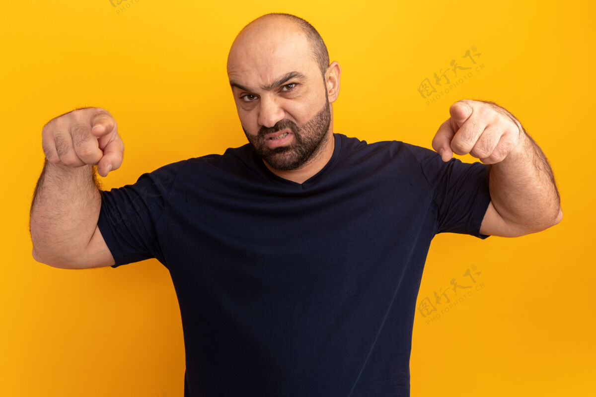 手指愤怒的留着胡子的男人穿着海军蓝t恤 用食指指着橙色的墙胡子站手势