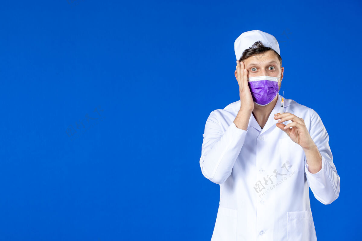 套装前视图中的男医生穿着医疗服和面具举行注射蓝色医院注射药品