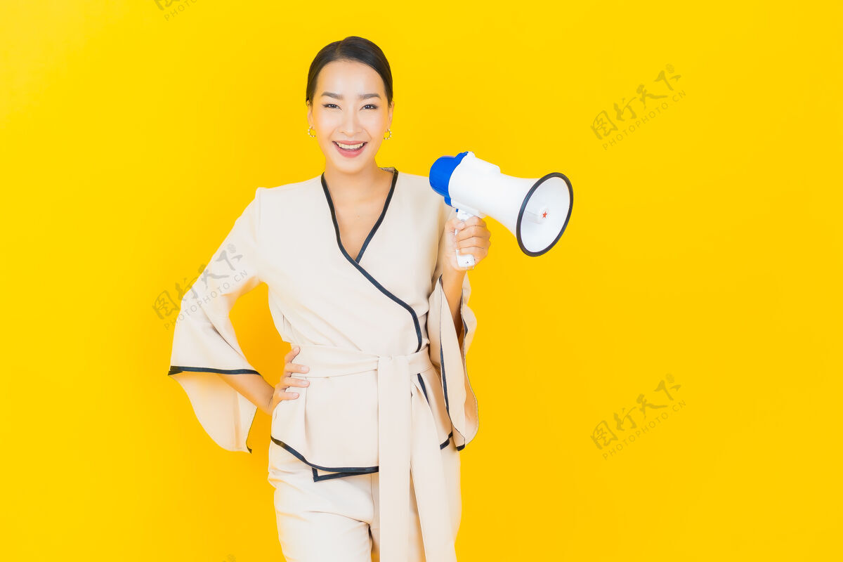 手持黄墙上挂着一幅美丽的亚洲商界年轻女子的画像 她拿着扩音器在交流成功主管注意