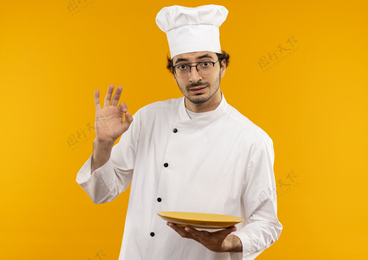 烹饪年轻的男厨师穿着厨师制服 戴着眼镜 拿着盘子 摆出一副很好的姿势男厨师穿