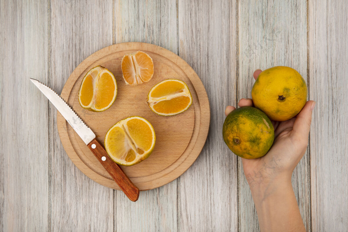手女性手拿橘子的俯视图 半个橘子被隔离在木制的厨房板上 刀放在灰色的木制表面上饮食柑橘板