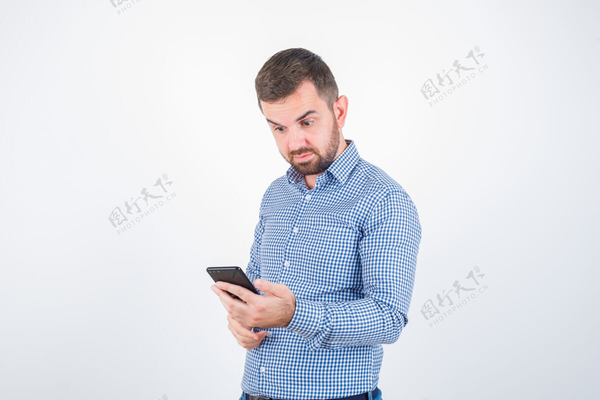 手机男青年穿着衬衫 牛仔裤 看着手机 神情迷惑不解 前视问题小伙子困惑