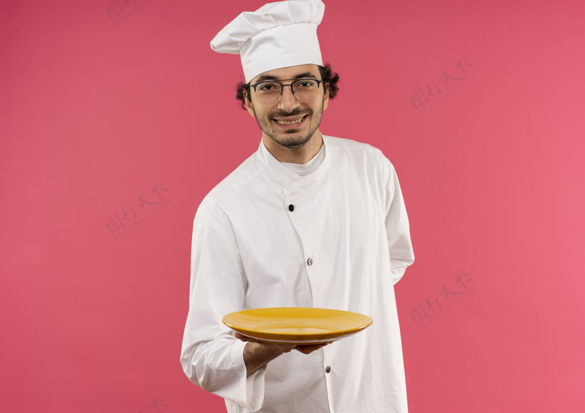 戴着面带微笑的年轻男厨师穿着厨师制服 戴着眼镜拿着盘子制服粉红眼镜