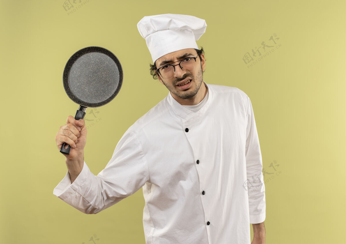 男人愤怒的年轻男厨师穿着厨师制服 戴着眼镜举起煎锅眼镜烹饪厨师