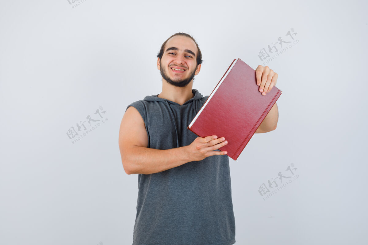 抱着年轻的男性穿着无袖连帽衫拿着书 一边摆姿势 看起来很开心 正面照乐观站立商人
