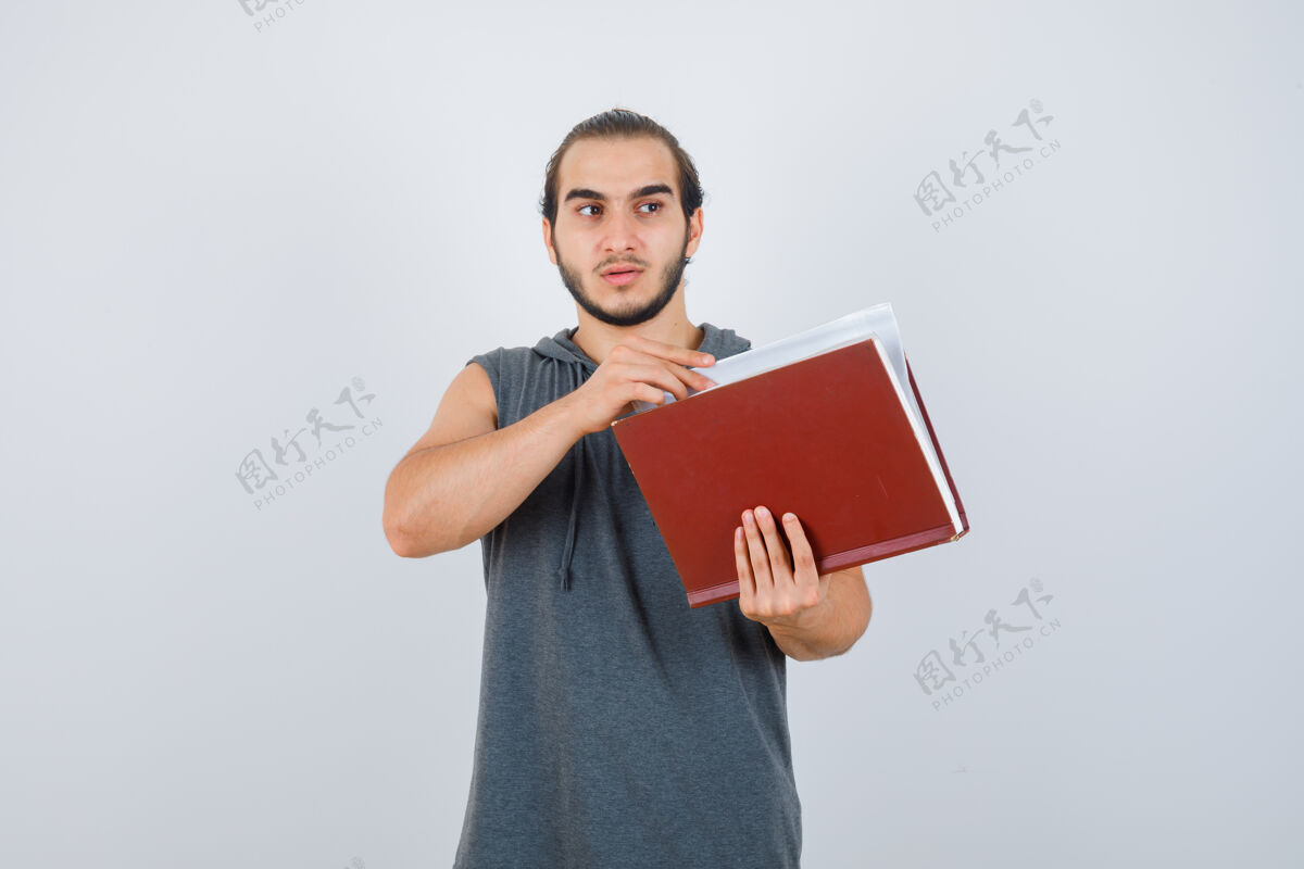 年轻年轻的男性拿着书 穿着无袖连帽衫望向别处 神情沉思前视图活跃人肖像