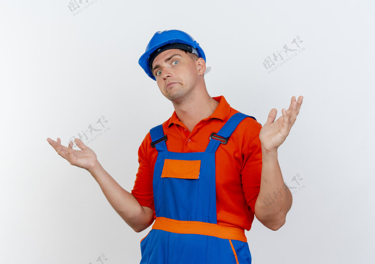 头盔困惑的年轻男性建筑工人穿着制服和安全帽摊开双手蔓延年轻手