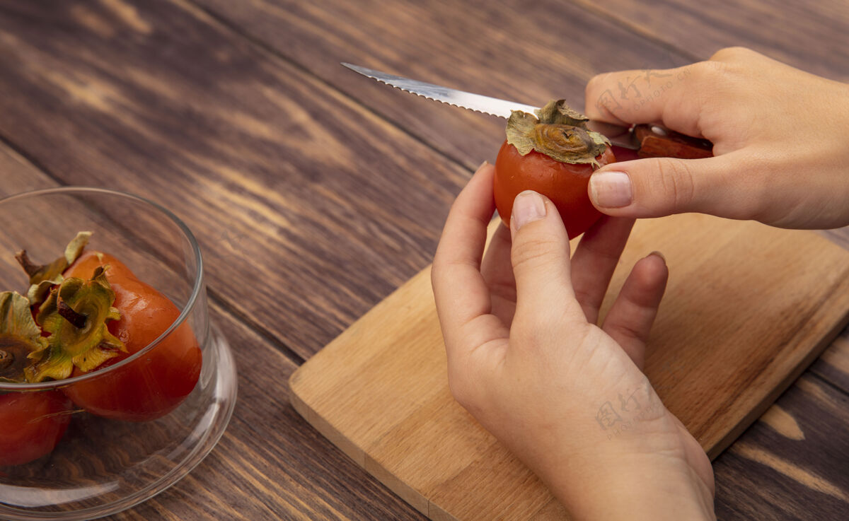 甜点俯视图中的女性手切割新鲜和柔软的柿子在木制厨房板上用刀在木制表面水果午餐女