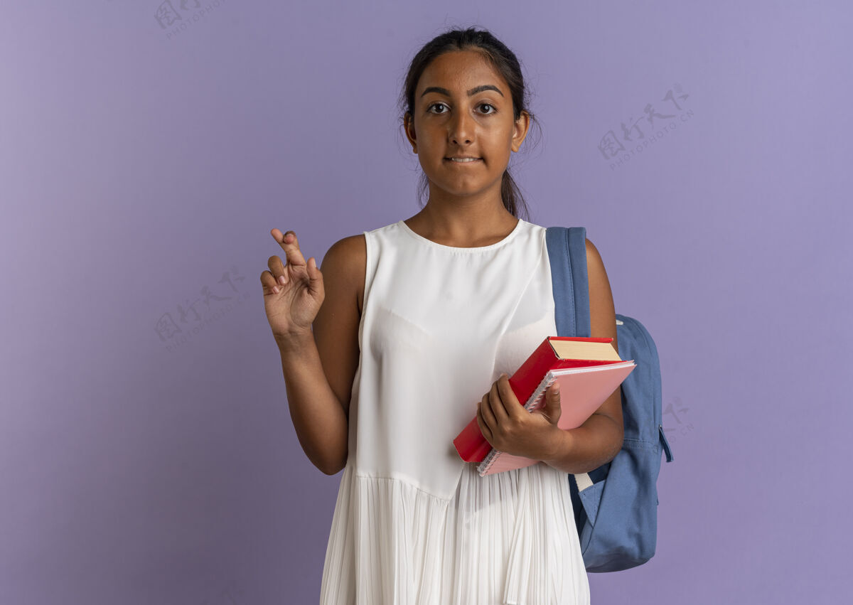 手指关心的年轻女学生 背着书包 拿着笔记本 交叉着手指十字架手握关心