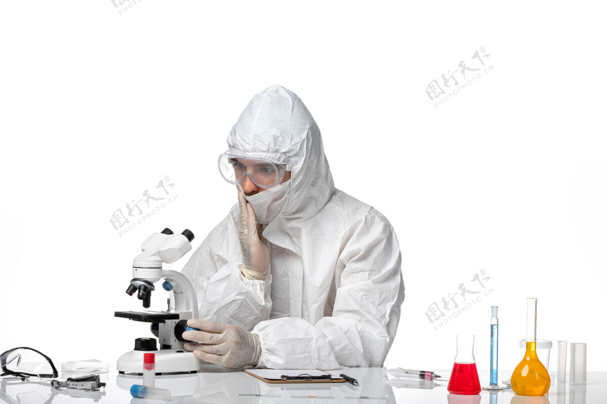 防护正面图：男医生穿着防护服 戴着面罩 在白色办公桌上使用显微镜使用男性专业人员