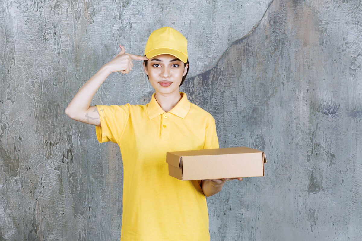 年轻人穿着黄色制服的女服务人员手里拿着一个纸板箱 看上去既困惑又体贴计划姿势梦想