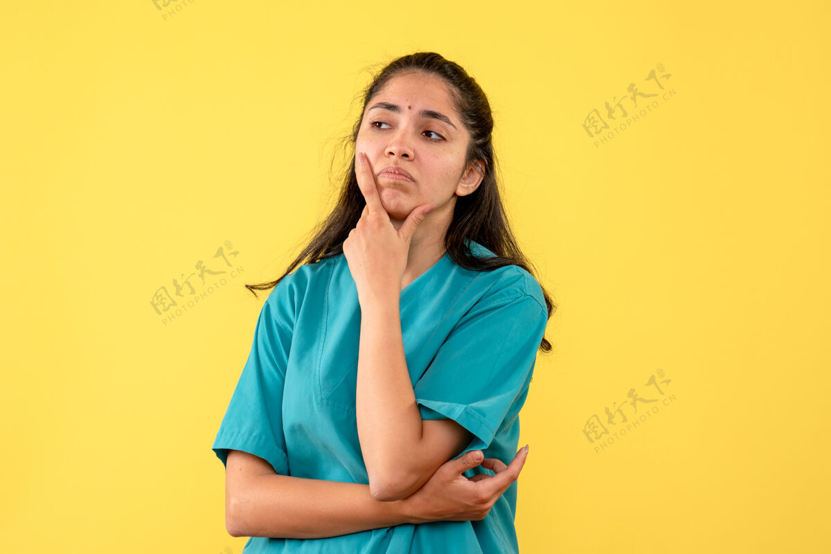 模特前视图失望的女医生穿着制服把她的手放在她的下巴上黄色孤立的背景制服正面手