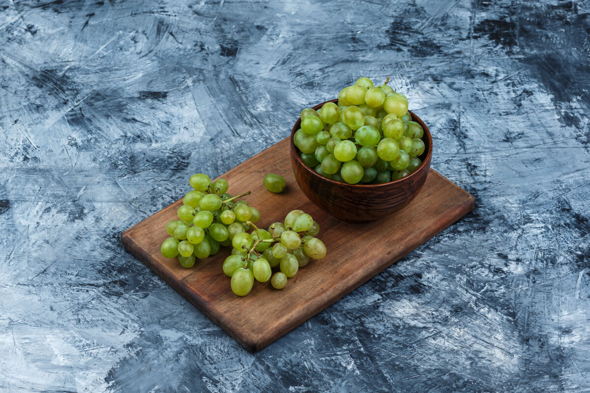 叶子在深蓝色大理石背景的砧板上高角度观看白葡萄碗水平角度葡萄藤葡萄酒