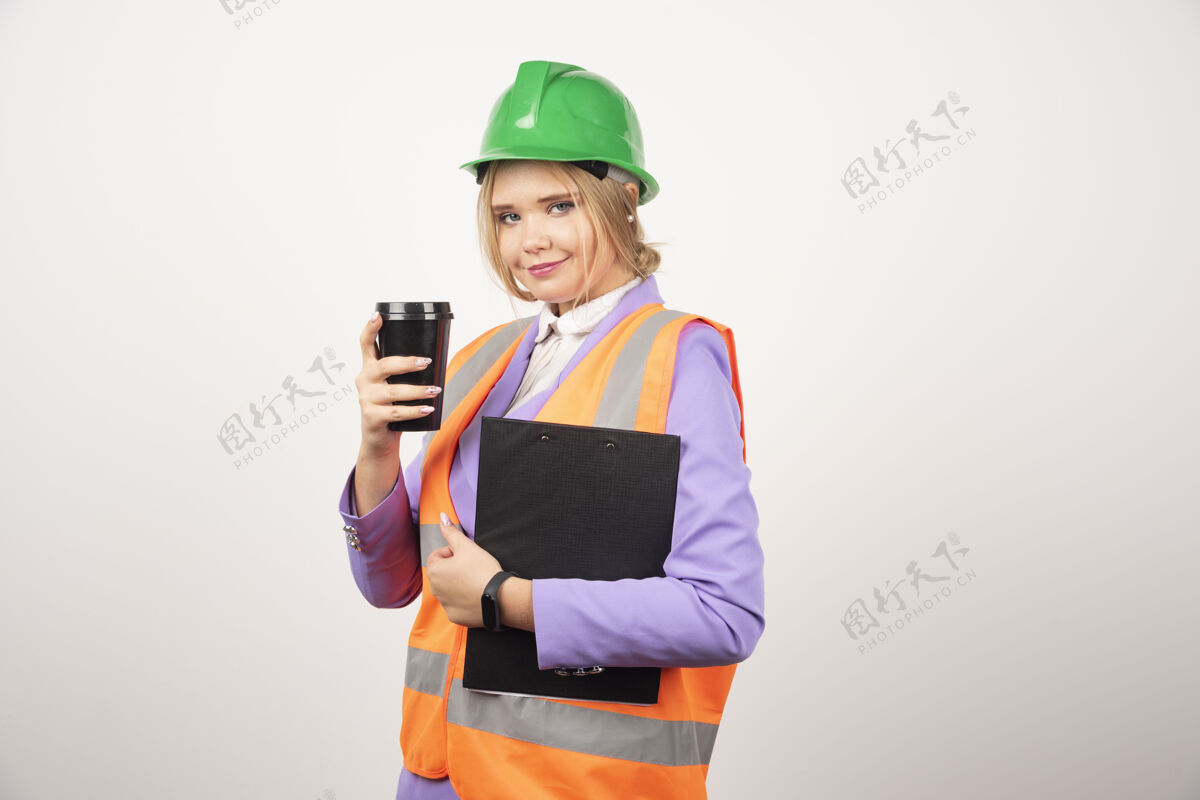 杯子穿着制服的女工业工程师 白墙上有剪贴板和黑杯子女士工作模型