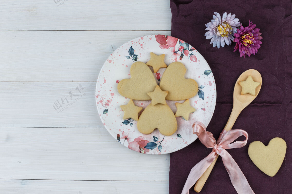 甜点平铺饼干在盘子和木制勺子上 木制和纺织品背景上有花水平面包屑纺织品早餐