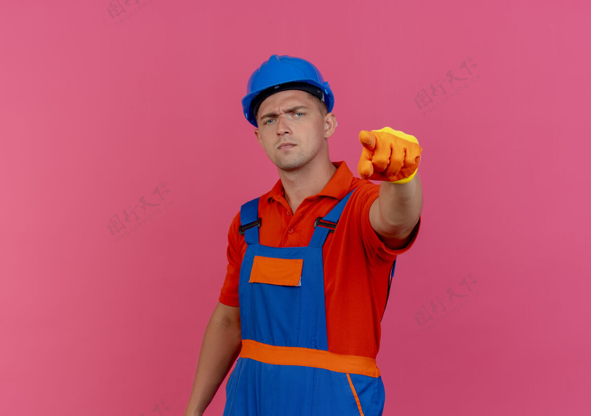 建筑工人自信的年轻男性建筑工人穿着制服 戴着手套戴着安全帽 向你展示姿势自信穿着手套