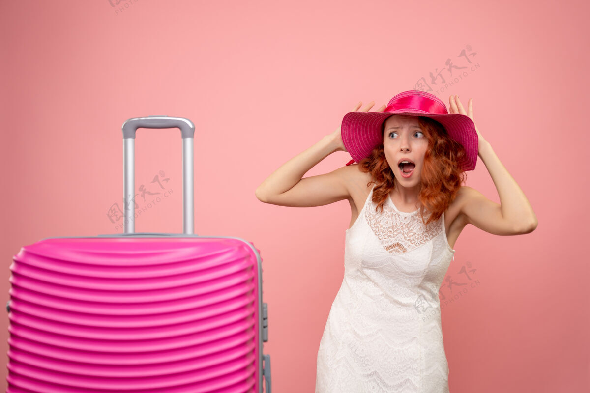 夏天年轻的女性游客与粉红色的帽子和粉红色的墙壁上的包的正面视图可爱包航行
