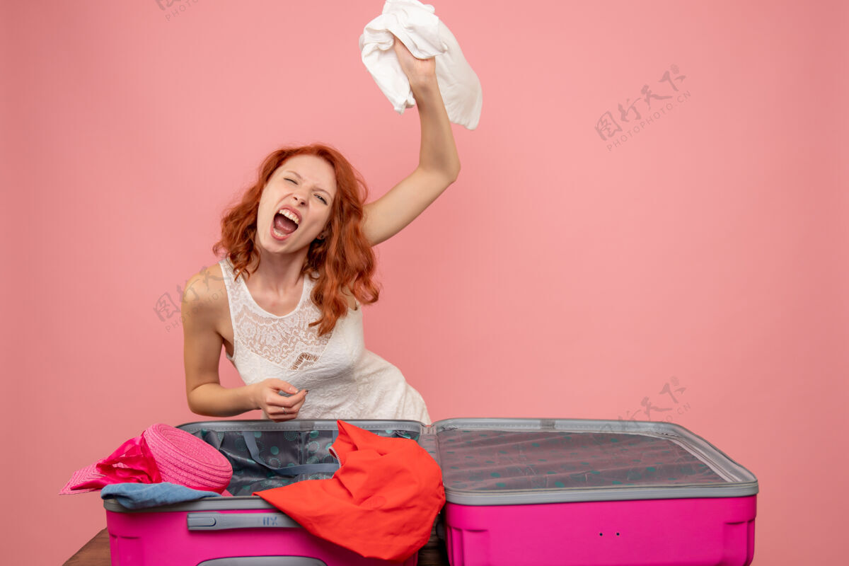 假期年轻女子怒气冲冲地把衣服扔在粉色墙上的正面图快乐坐着扔