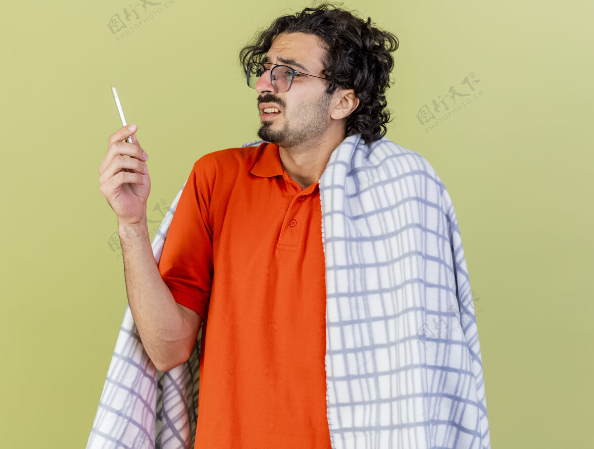 体温计一个年轻的白种人 戴着一副格子布包裹的眼镜 拿着橄榄绿的墙上隔离着的温度计包裹穿着格子