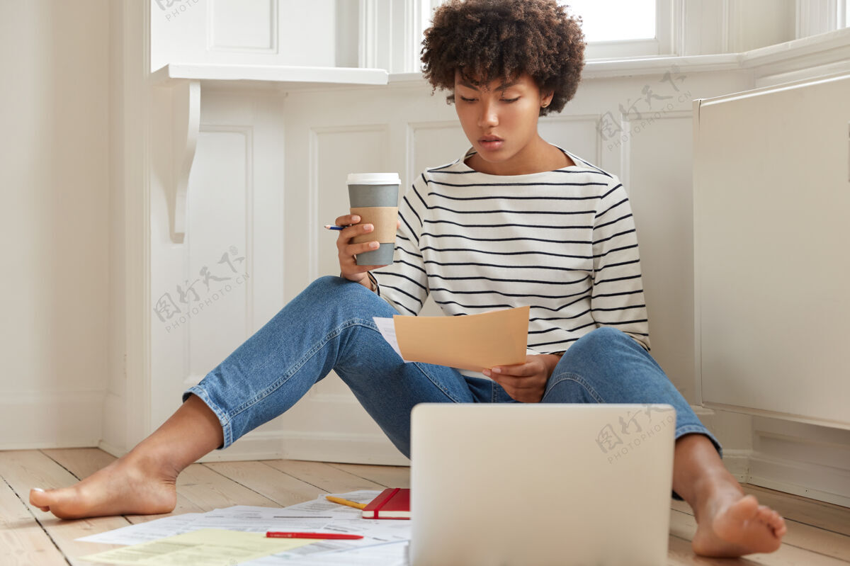 电脑严肃的黑皮肤女经济学家在创业项目上思考 持纸质文件个人教科书赤脚