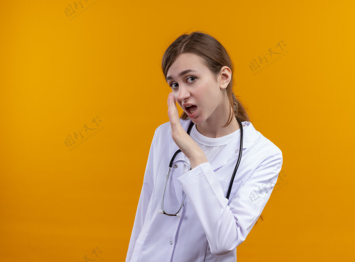 年轻穿着医用长袍和听诊器的年轻女医生低声说 把手放在靠近嘴巴的隔离橙色墙壁上 留有复印空间长袍耳语听诊器