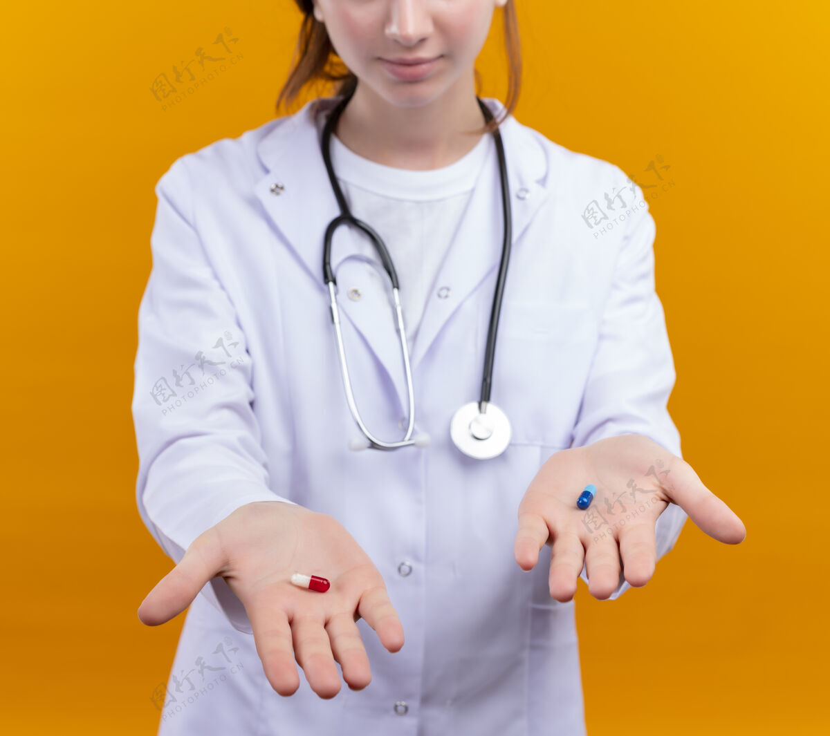 伸展年轻的女医生穿着医用长袍和听诊器在隔离的橙色墙上伸展医用胶囊医生女长袍