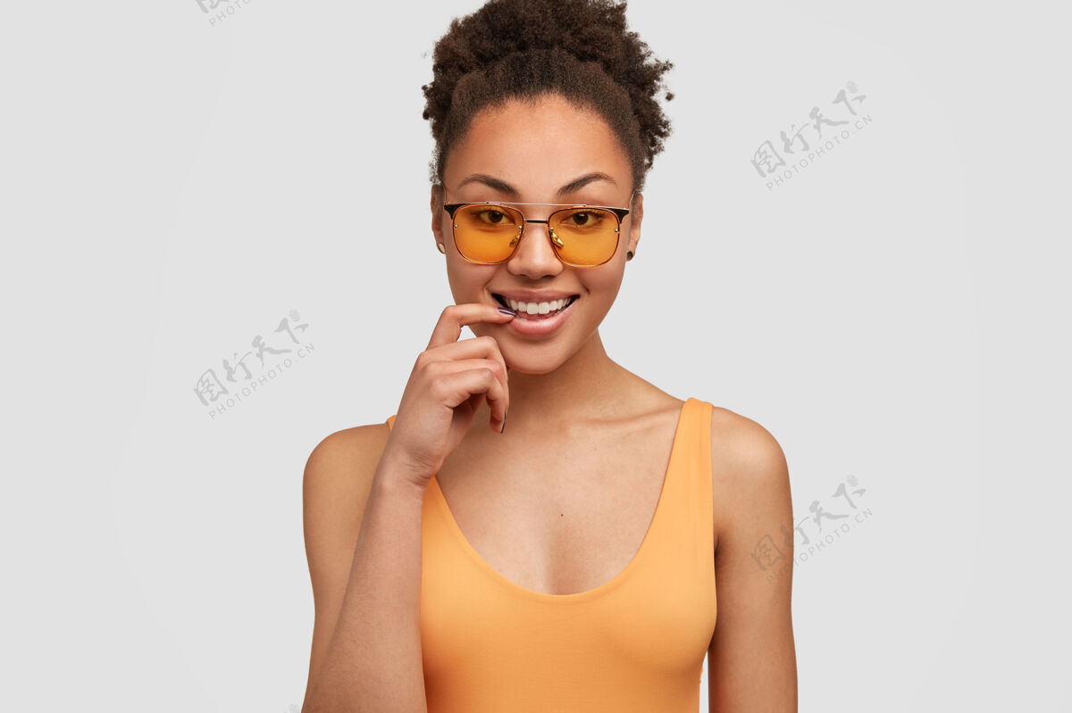 面部迷人的积极的非裔美国女人有着牙齿般的微笑 健康的深色皮肤 食指靠近牙齿外观位置人