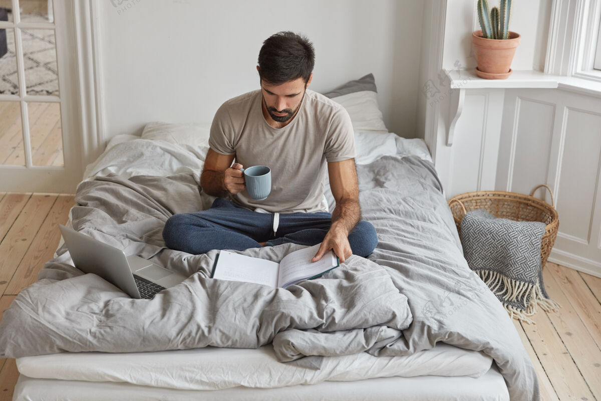 设备年轻白种人的形象是早上喝咖啡 盘腿坐在床上床卧室作家