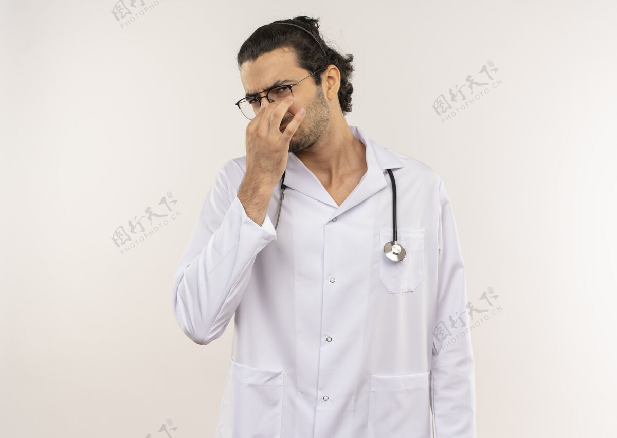 年轻神经质的年轻男医生 戴着眼镜 穿着白色长袍 带听诊器 在隔离的白墙上闭着鼻子 留着复印空间吱吱光学封闭