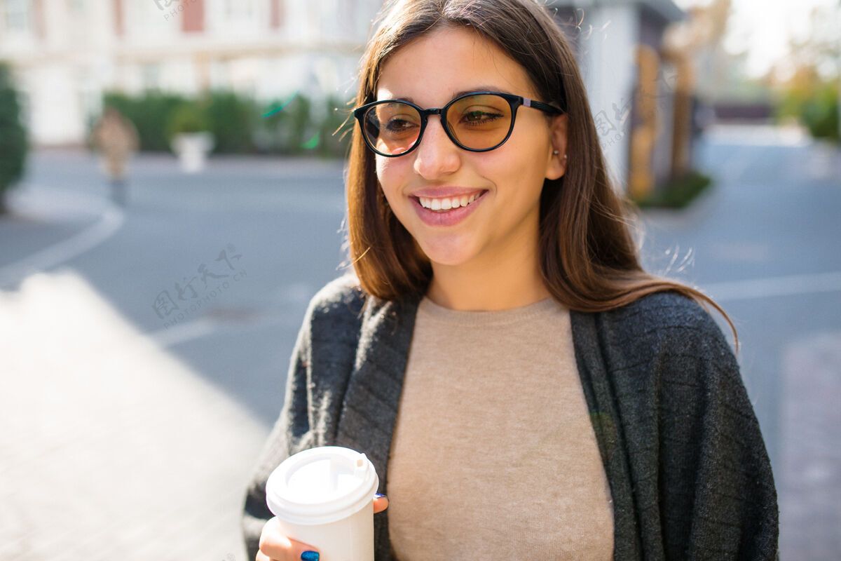 快乐带着太阳镜和咖啡去街上散步的漂亮时髦女人情感可爱快乐的女人
