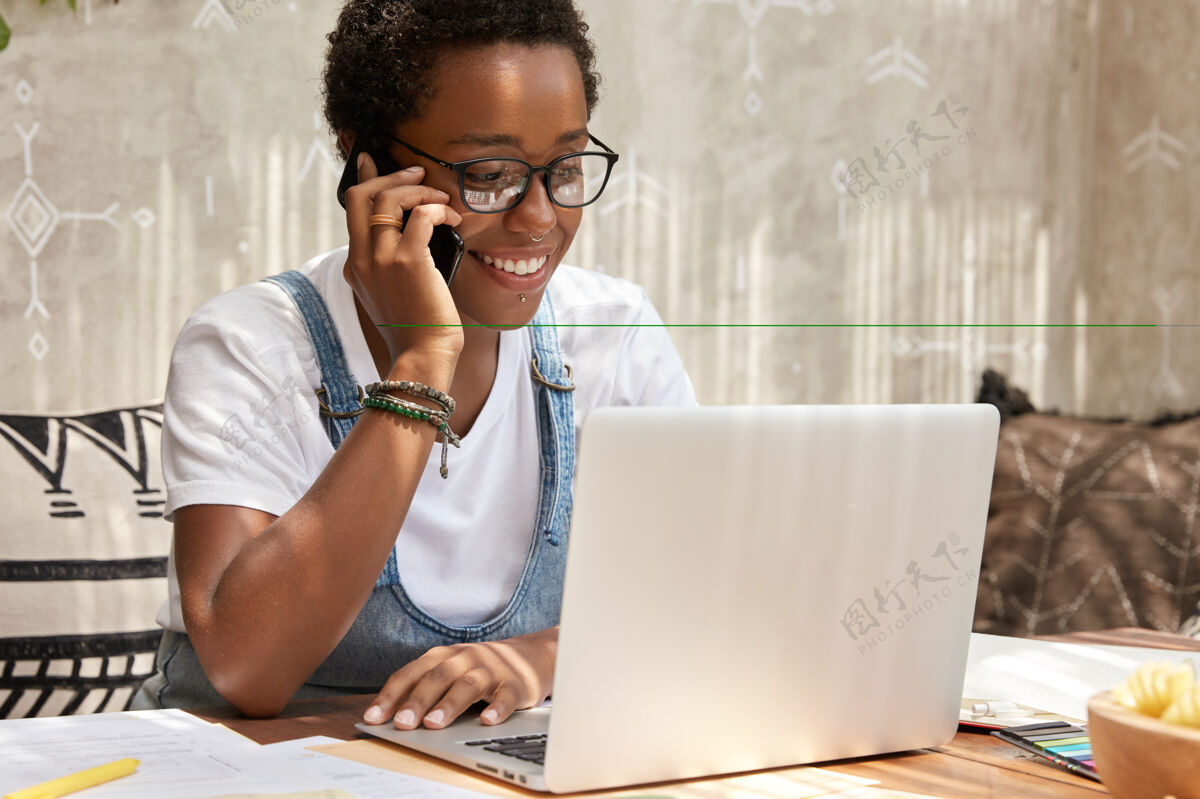 专业时尚的非裔美国女人打电话智能手机看笔记本电脑 更新软件坐着自由职业者人类