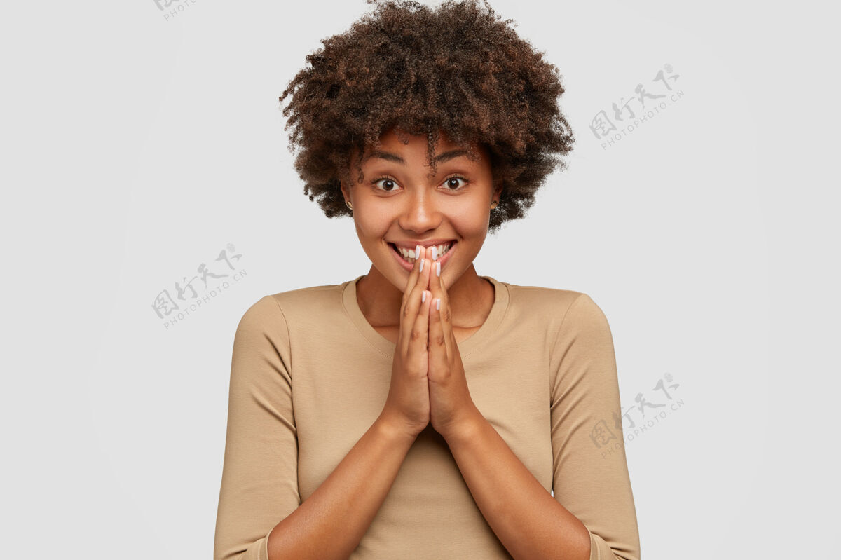 墙喜怒无常的黑皮肤女孩有着牙齿般的微笑 保持双手祈祷的姿势姿势满意反应
