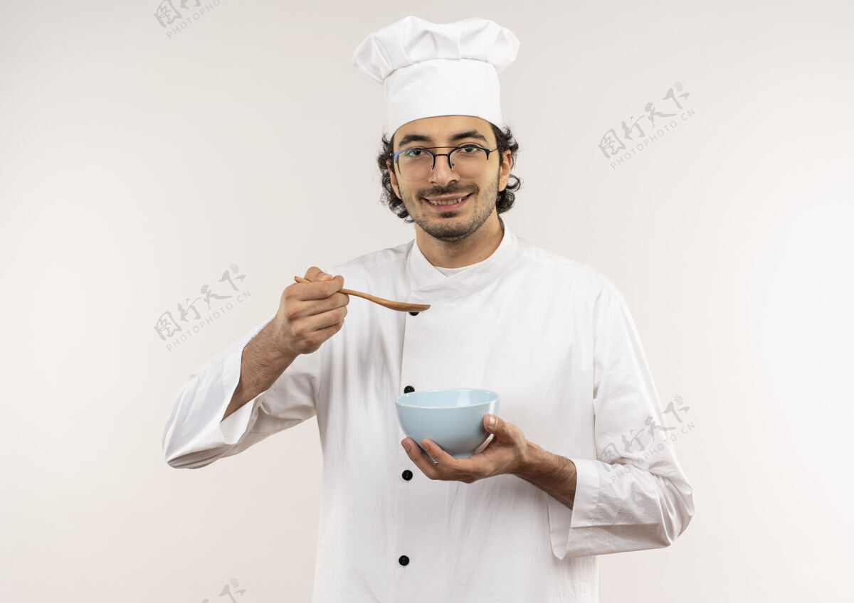 拿着年轻的男厨师穿着厨师制服 戴着眼镜 拿着勺子 碗被隔离在白色的墙上厨师碗穿