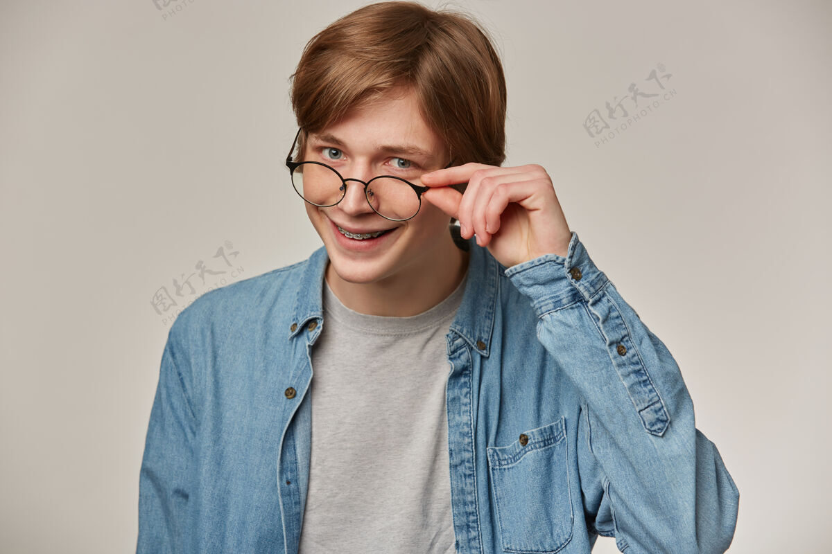 20多岁帅气的男人 金发帅哥穿着牛仔衬衫 戴着眼镜戴着牙套抚摸着眼镜 微笑着情感概念男性颜色服装
