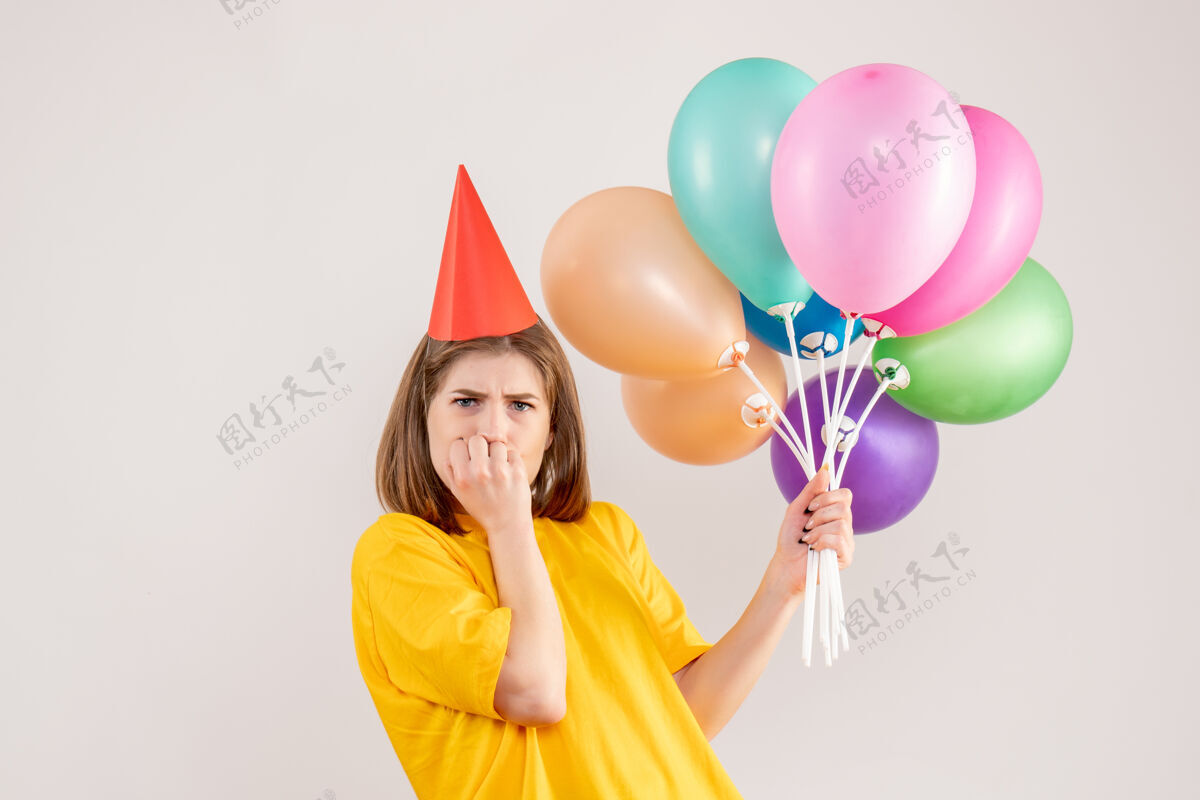 看法手持彩色气球的年轻女子紧张地站在白色的地面上庆祝情感丝带