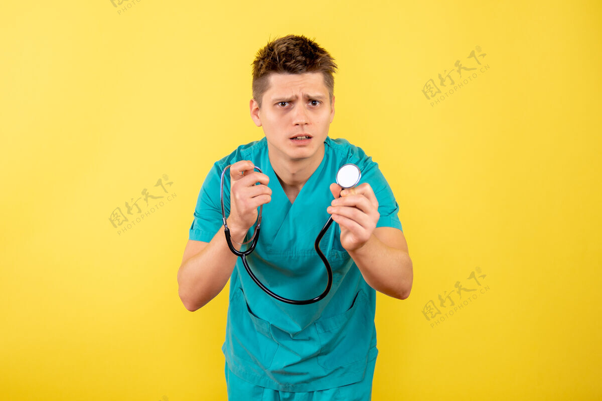 成人前视图年轻男医生穿着医疗服 黄色背景上带听诊器医院男性健康