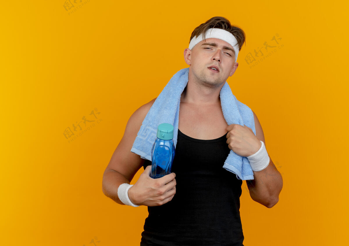 男人自信的年轻帅气的运动型男人戴着头带和腕带 脖子上围着毛巾 拿着水瓶和毛巾 橙色上有单独的复制空间水穿头带