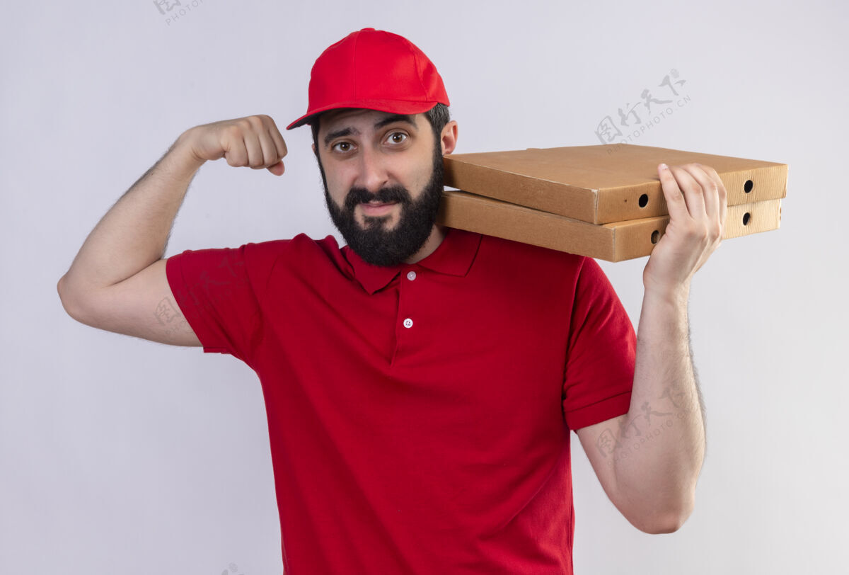 红色自信的年轻英俊的白人送货员身穿红色制服 头戴鸭舌帽 肩上扛着披萨盒 在白色衣服上做着强烈的孤立手势手势自信披萨