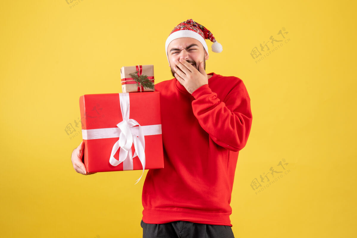 人黄色背景上手持圣诞礼物的年轻男性正面图年轻男性西装人