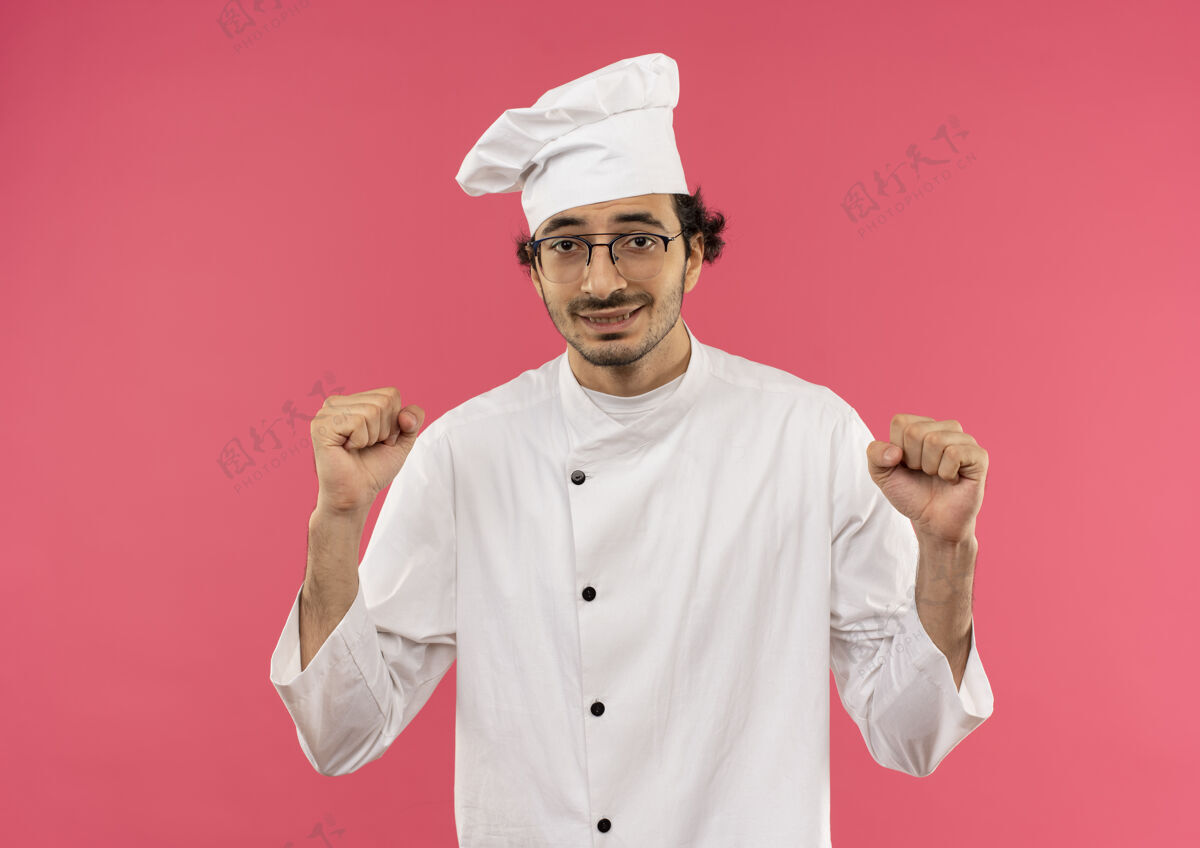 男性面带微笑的年轻男厨师穿着厨师制服 戴着眼镜 在粉红色的墙上展示着你的手势烹饪表演手势
