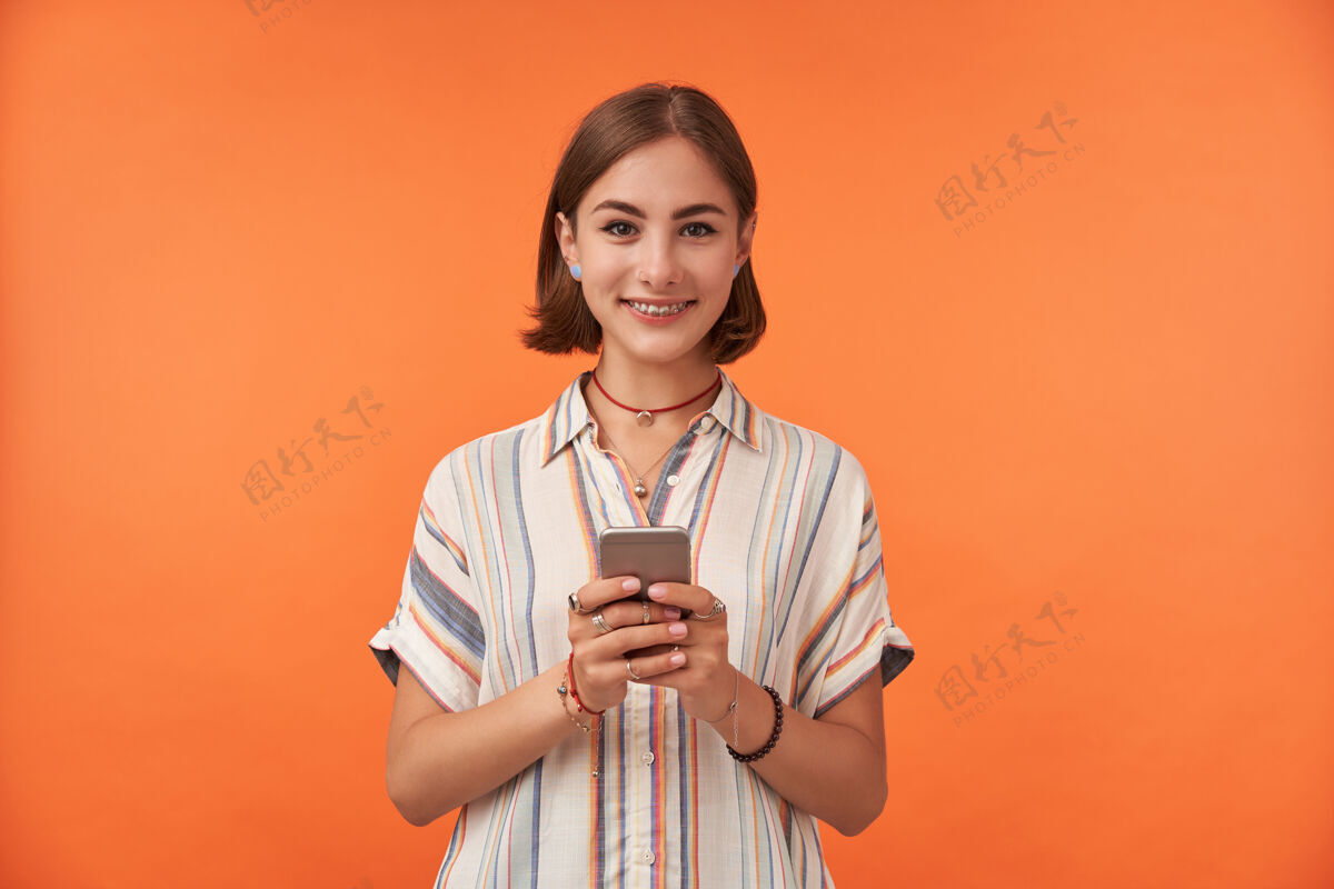 女人一个迷人的年轻女子微笑着 手持智能手机 穿着条纹衬衫 戴着牙套和戒指成人女性信息