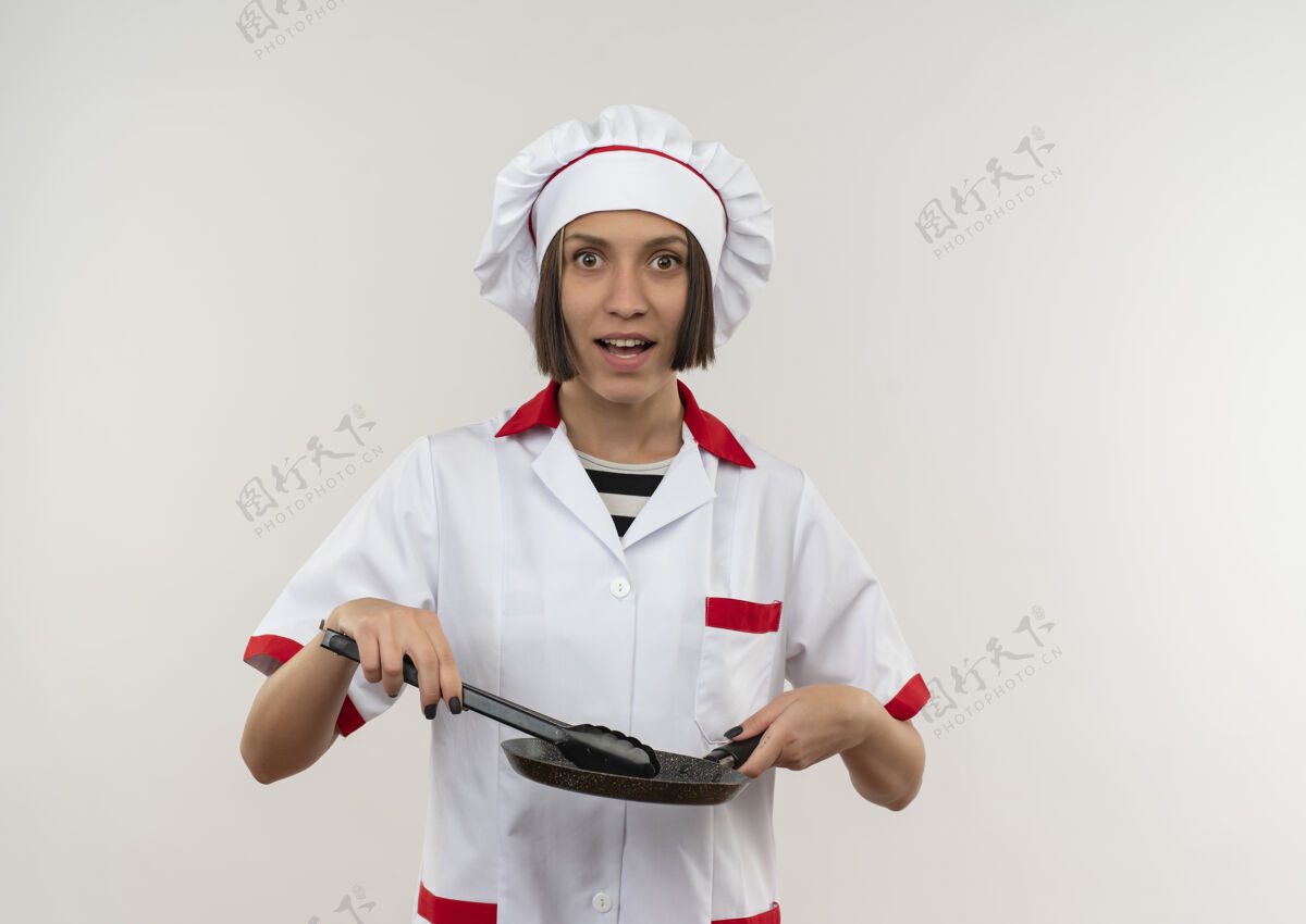 女印象深刻的年轻女厨师在厨师制服举行钳和煎锅隔离在白色与复制空间年轻制服印象
